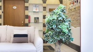 A lobby with a sofa, a potted plant, a door labeled "101", and a wall with a "Food" sign. - Arcobaleno Rooms (Cagliari)