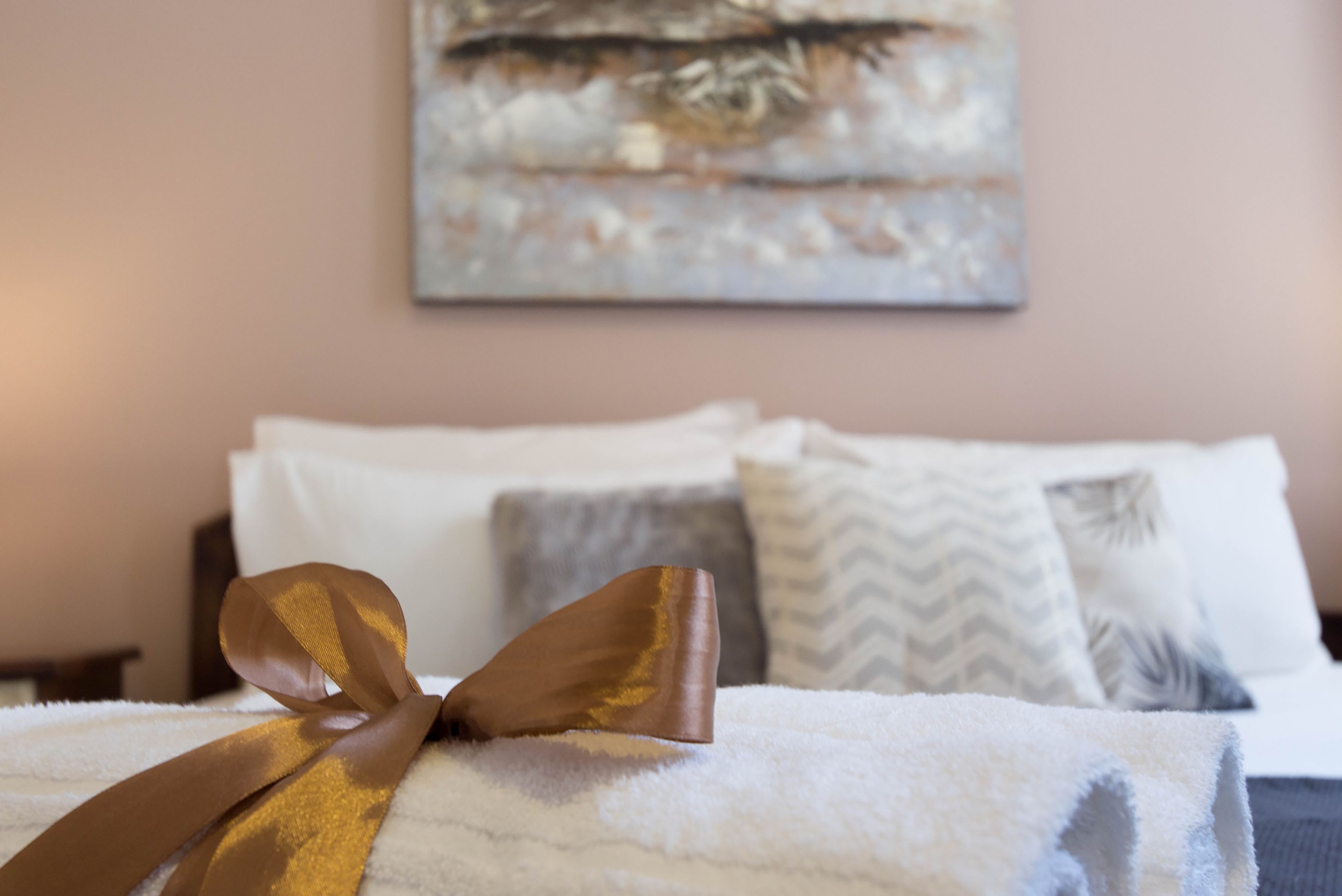 A neatly made bed with a golden ribbon, white pillows, and a textured wall art piece.