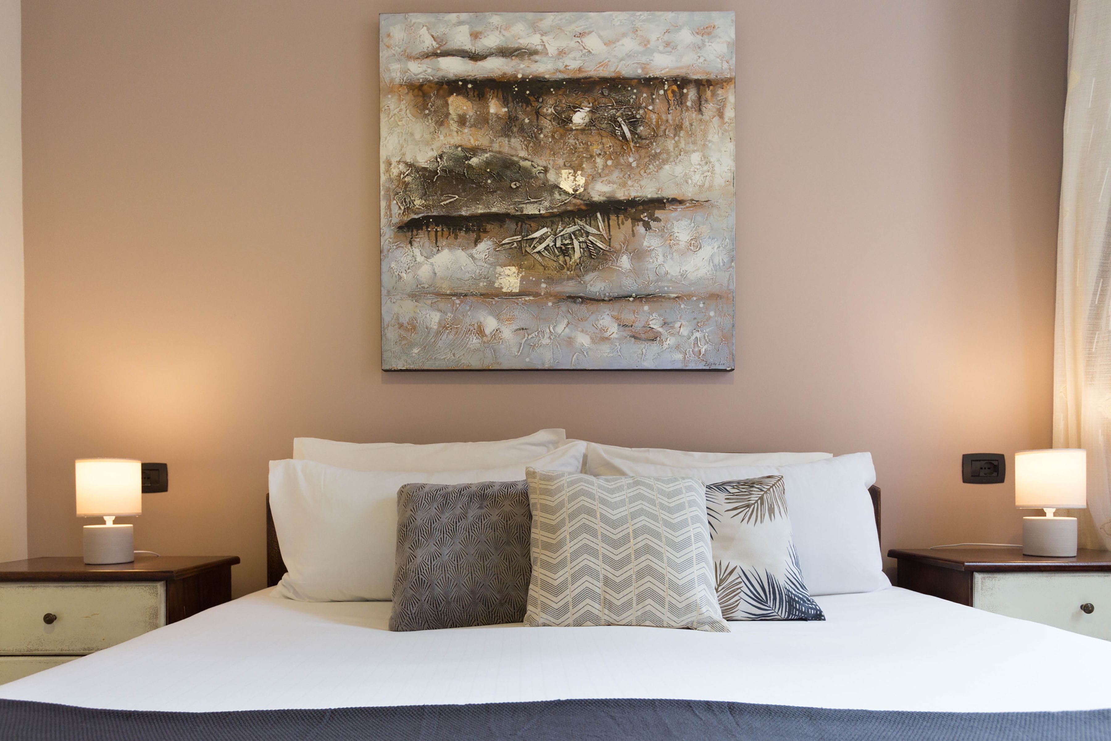 Une chambre à coucher avec un grand lit, deux tables de chevet et un tableau abstrait accroché au mur.