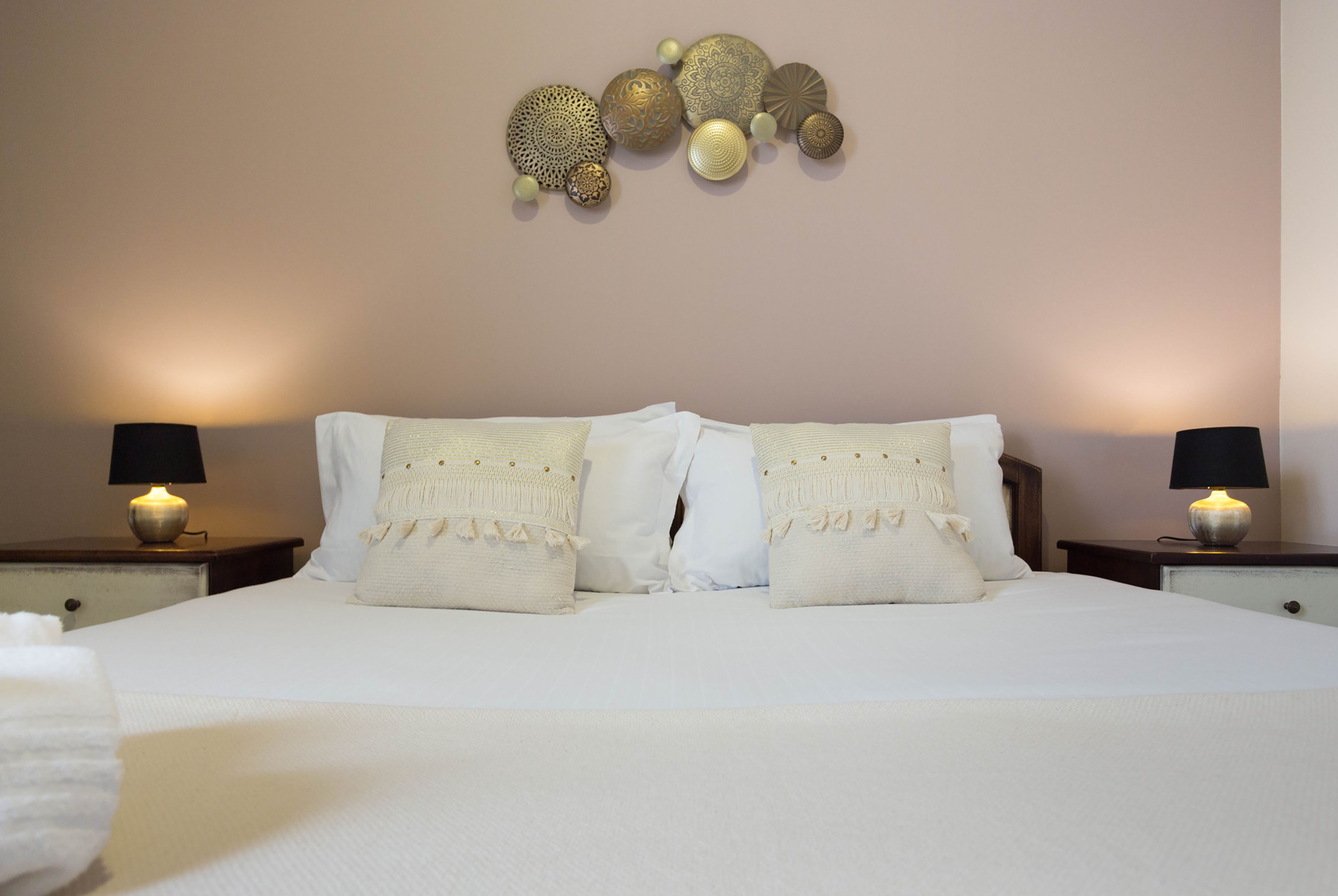 Een net opgemaakt bed met witte lakens en twee kussens, aan weerszijden voorzien van nachtkastjes met lampen.