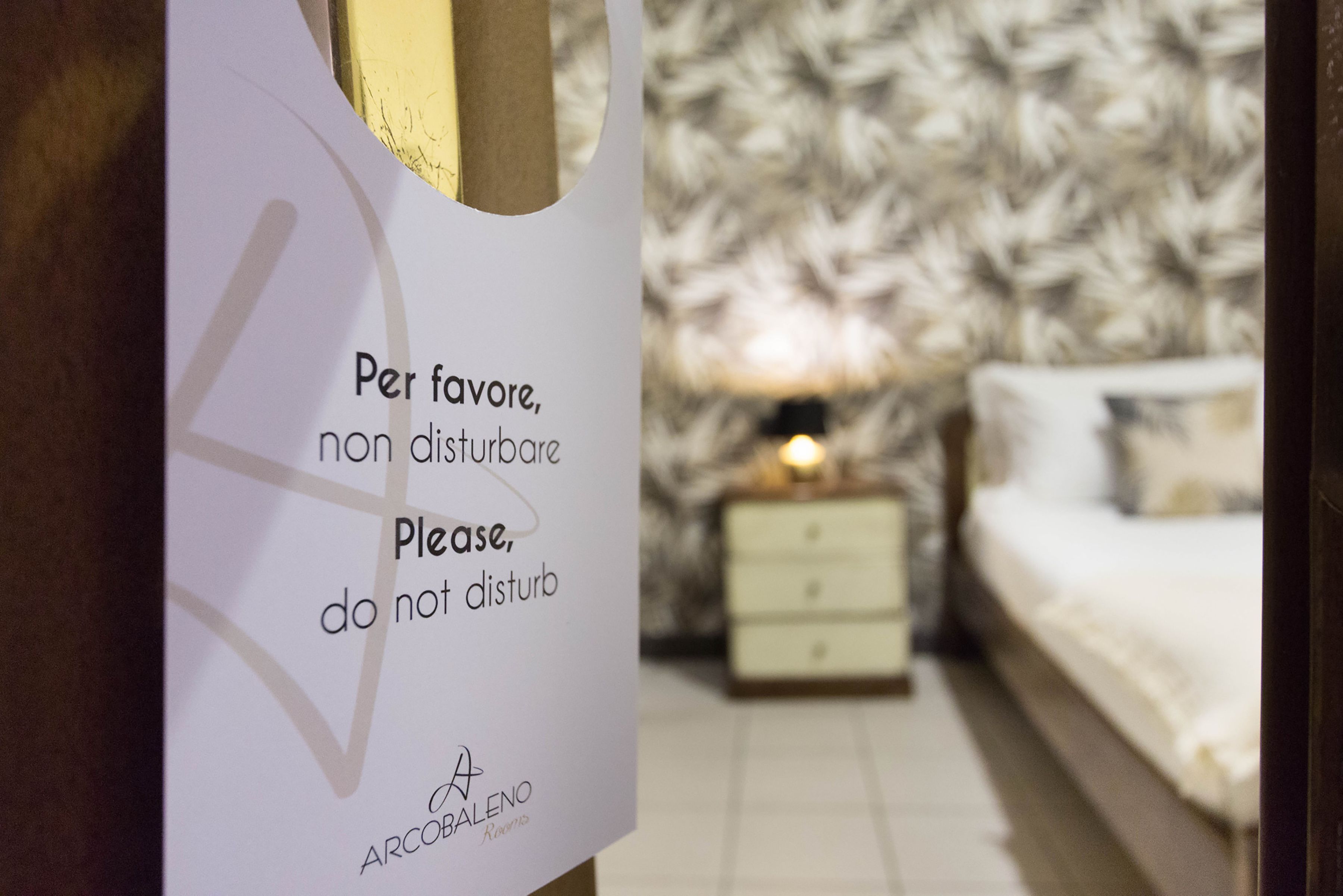 Un cartel en una habitación de hotel solicita no molestar. La habitación tiene una cama, una mesita de noche y una lámpara.