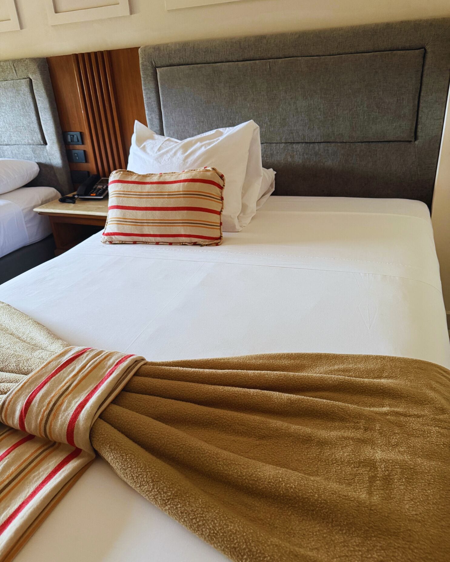 Une chambre d’hôtel avec un lit bien fait, un téléphone sur la table de chevet et un plaid à rayures.