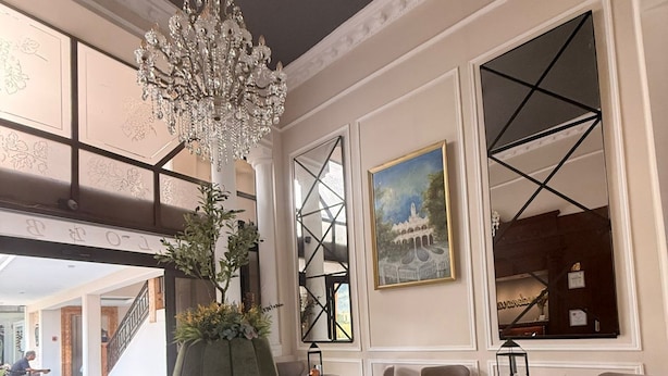 A spacious lobby with a green ottoman, a chandelier, and a large painting. - Hotel Residencial (Mérida)