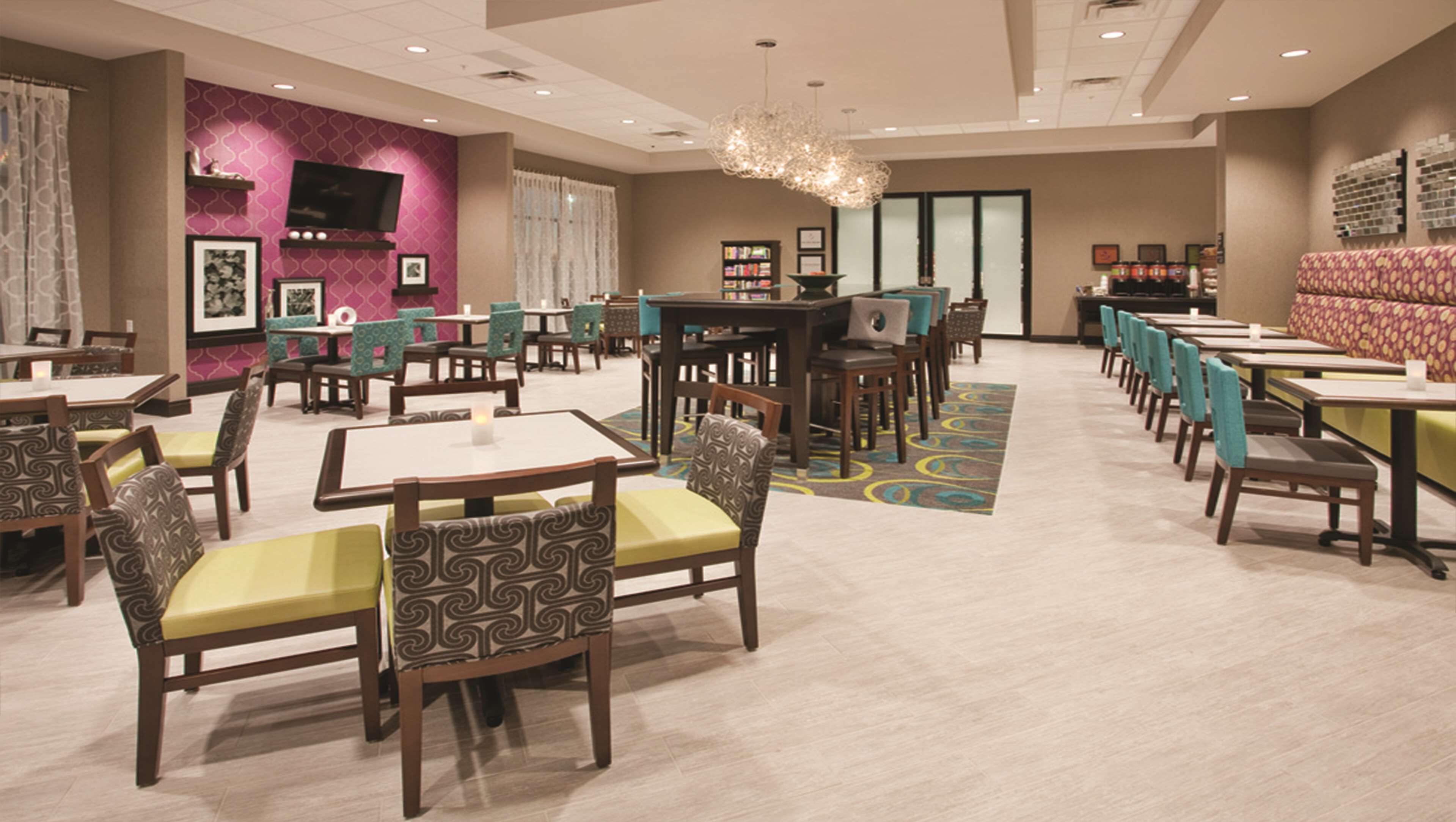 A hotel dining area with multiple tables and chairs, a bar, and a television.
