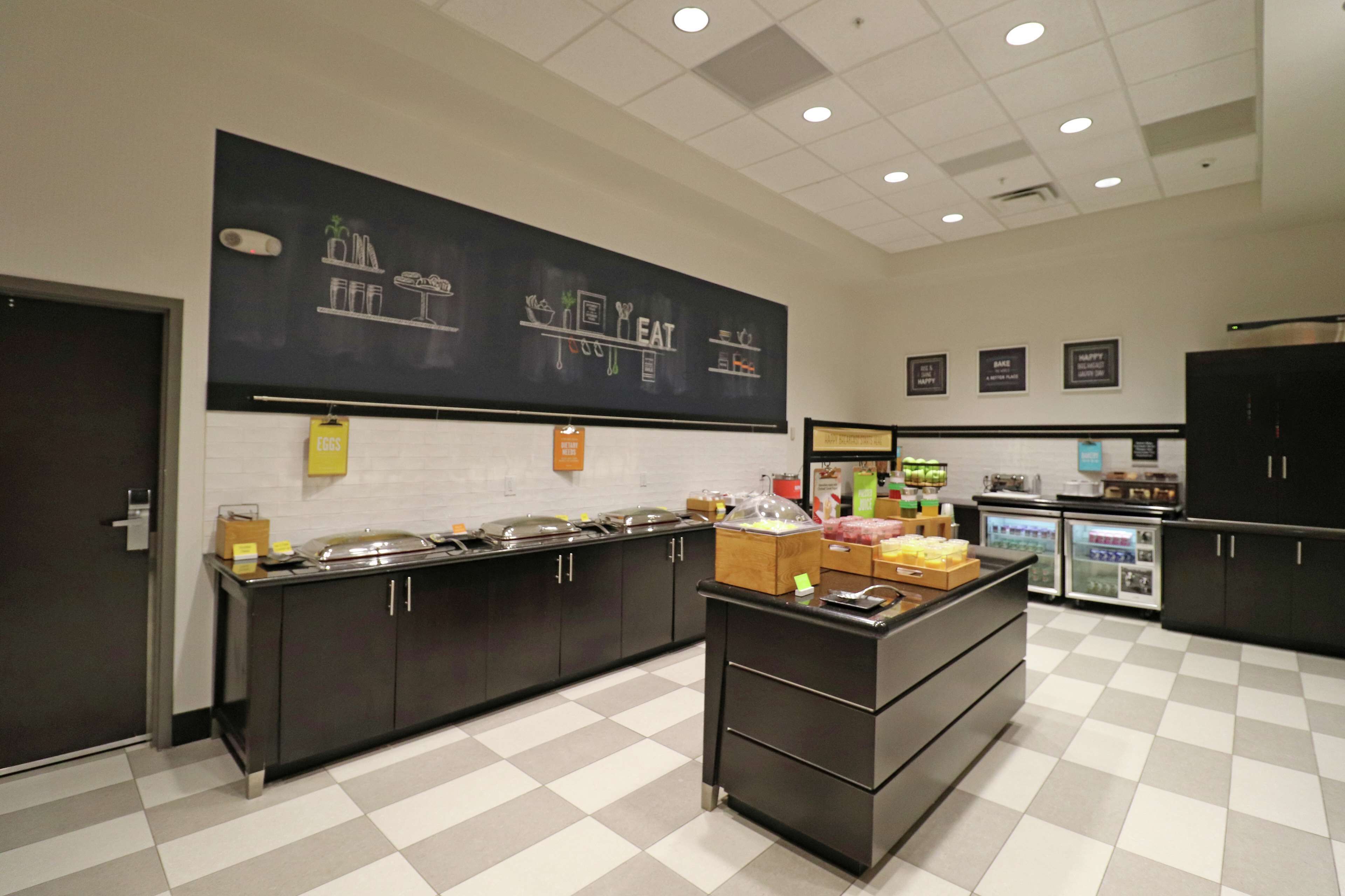 Une cuisine moderne avec un tableau noir où sont dessinés des motifs liés à l’alimentation, un buffet avec différents récipients contenant de la nourriture et un réfrigérateur.