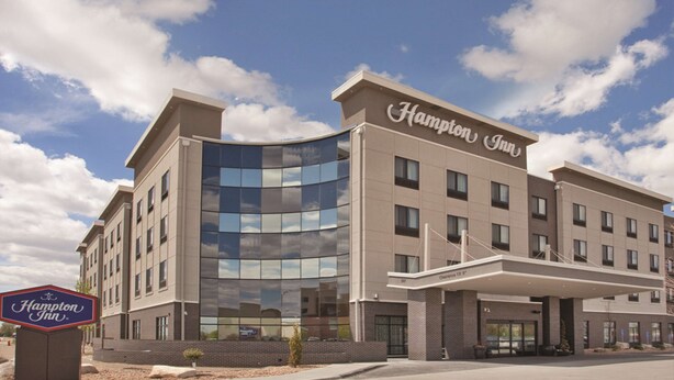 A Hampton Inn hotel with a modern design, featuring a curved glass facade and a covered entrance.