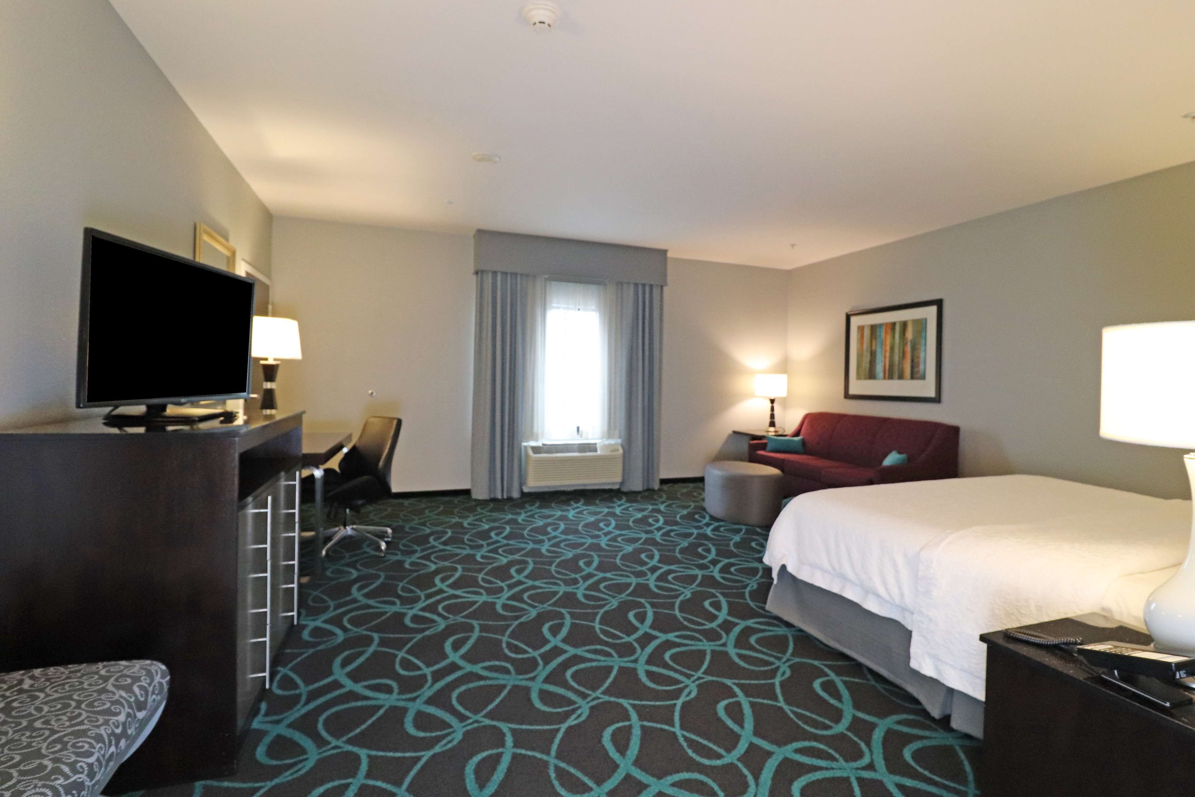 Habitación de hotel con una cama grande, un escritorio, un televisor de pantalla plana, una silla, un sofá y una ventana con cortinas.