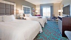 A hotel room with two beds, a desk, a TV, and a window with curtains.
