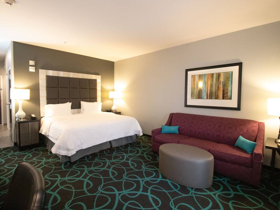 A hotel room with a bed, a red sofa, an ottoman, a desk, and a chair.