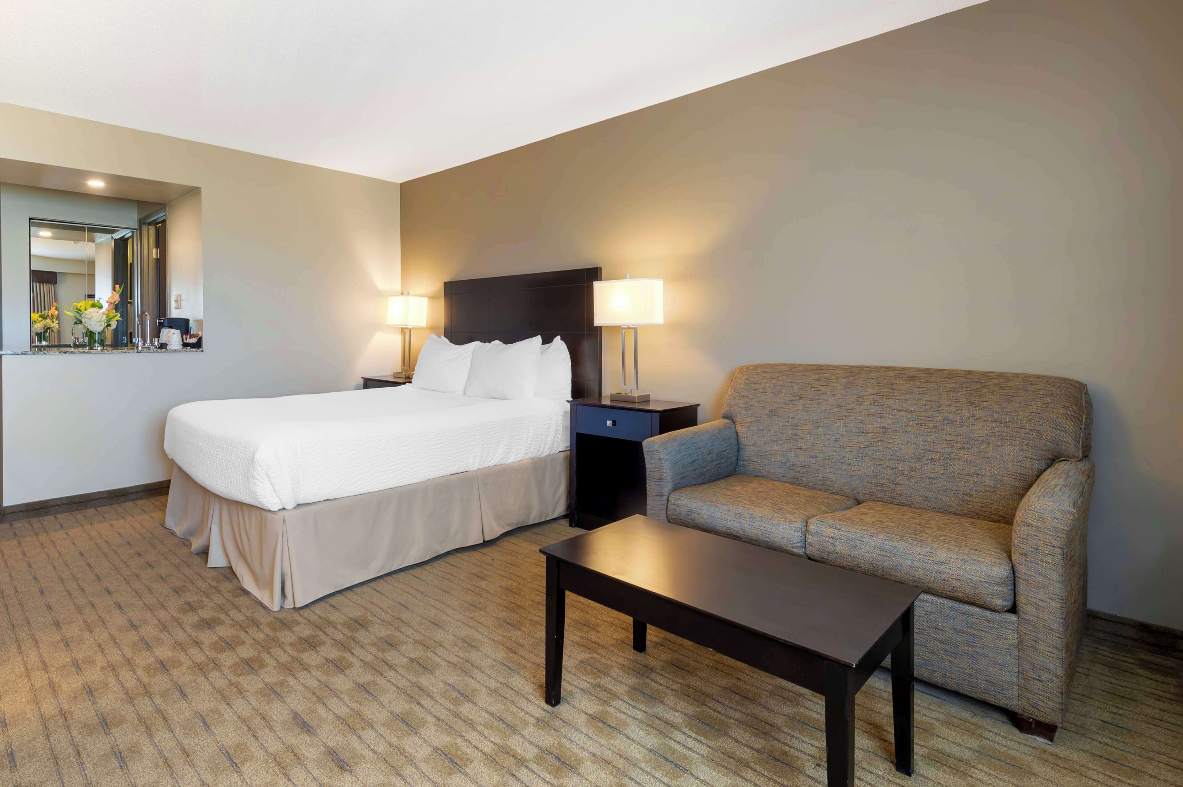 A hotel room with a bed, a sofa, a nightstand with lamps, and a mirror.