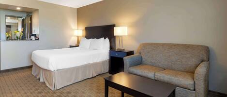 A hotel room with a bed, a sofa, a nightstand with lamps, and a mirror.