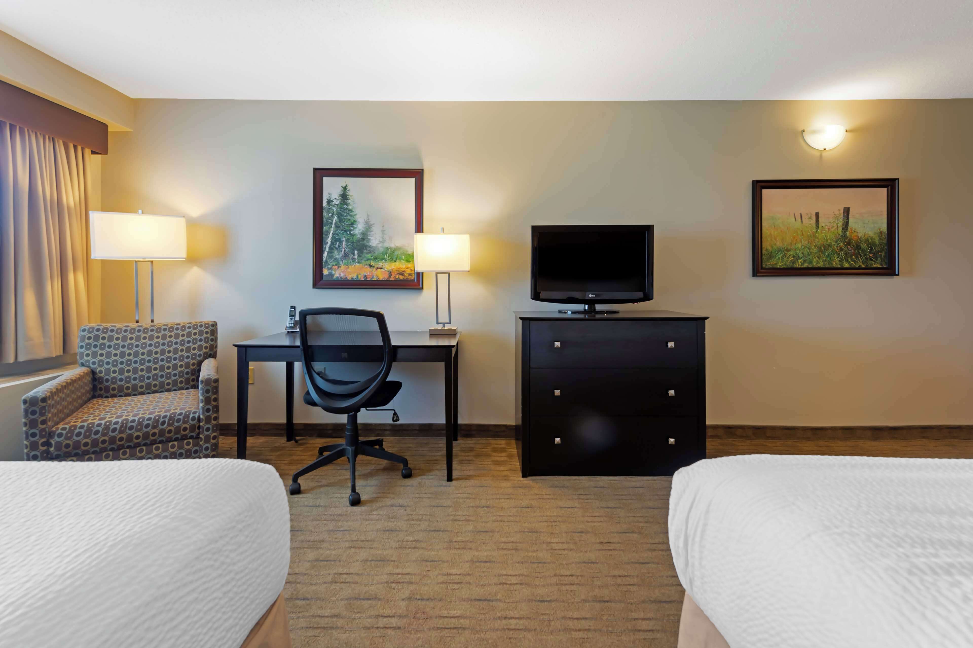 A hotel room with two beds, a desk with a chair, a television, and two wall-mounted lamps.