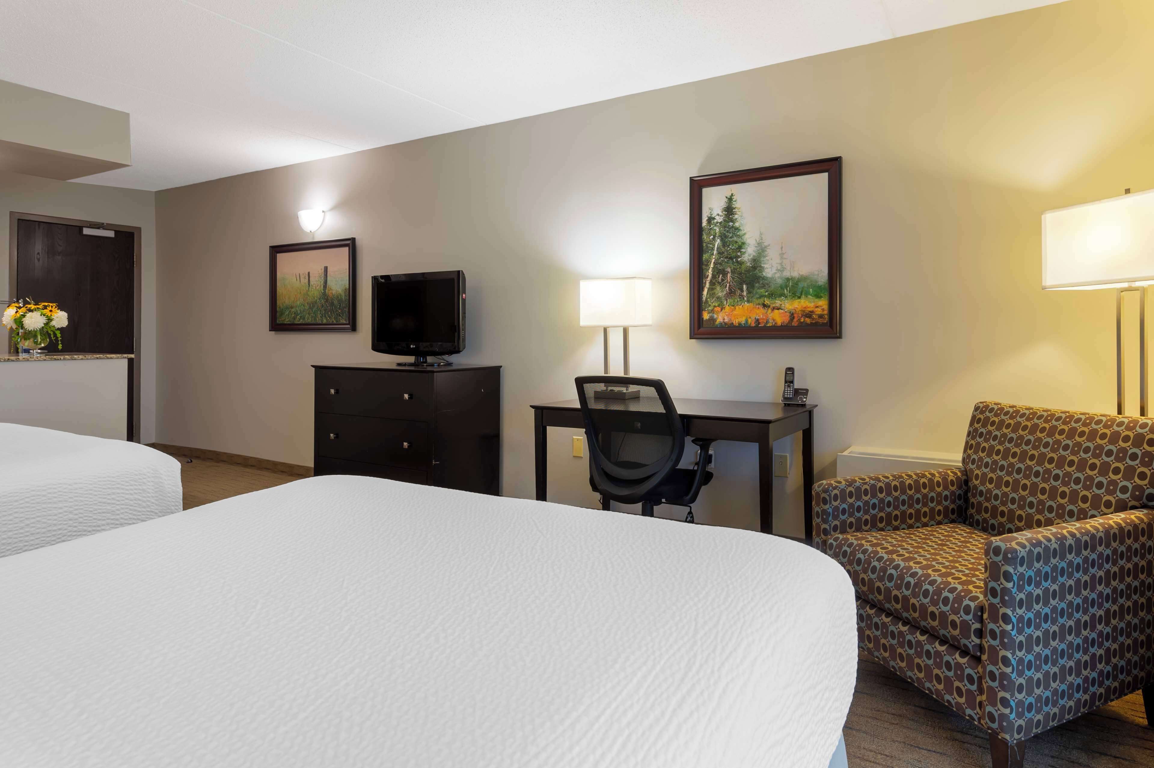 A hotel room with two beds, a desk with a computer, a chair, a TV, and a painting on the wall.