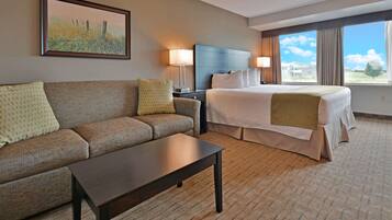 A hotel room with a bed, a sofa, a coffee table, and a painting on the wall.