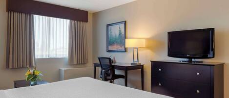 A hotel room with a large bed, a desk with a chair, a television, a lamp, and a painting on the wall.