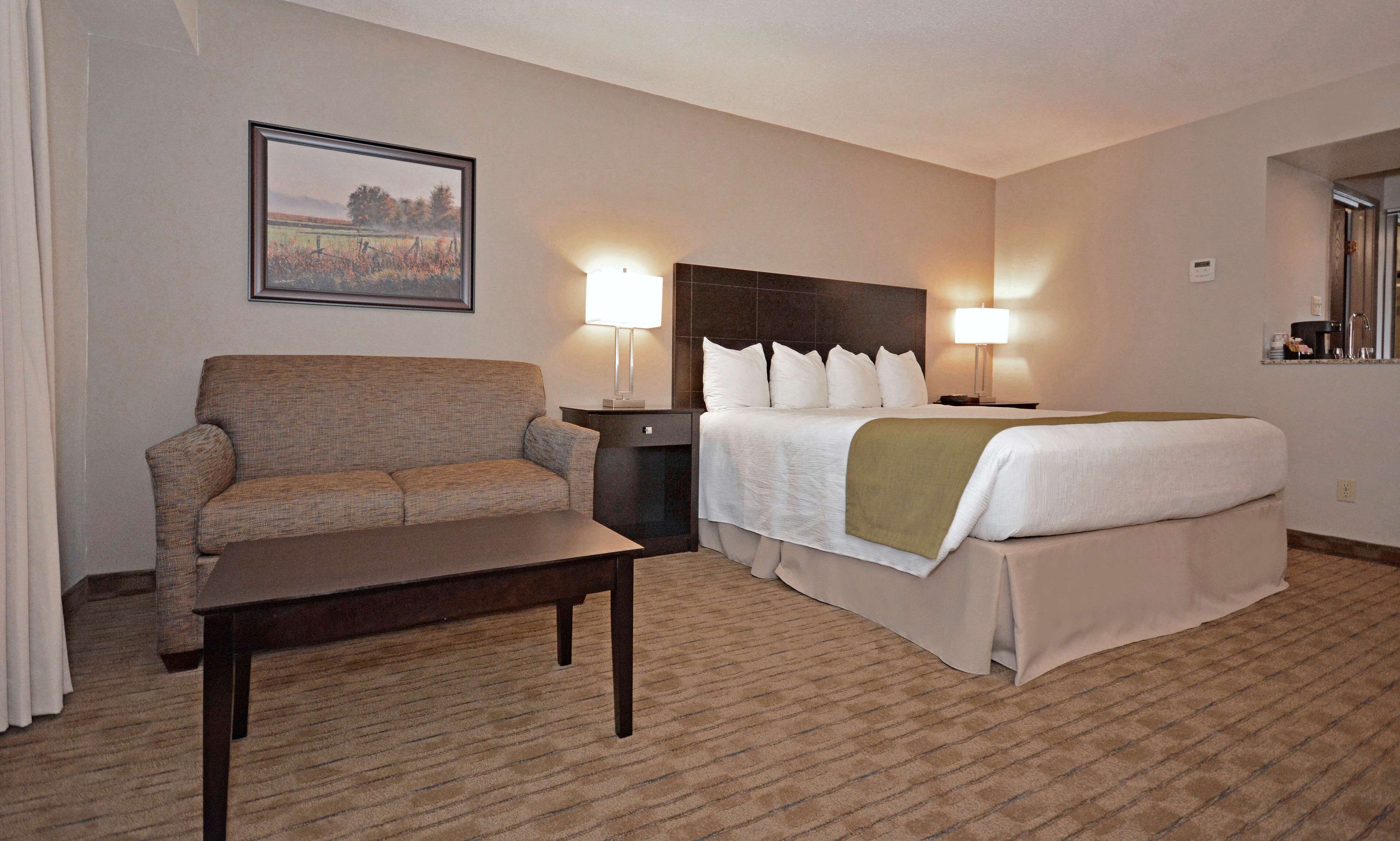 Quarto de hotel com cama, sofá, mesa de cabeceira e abajur.