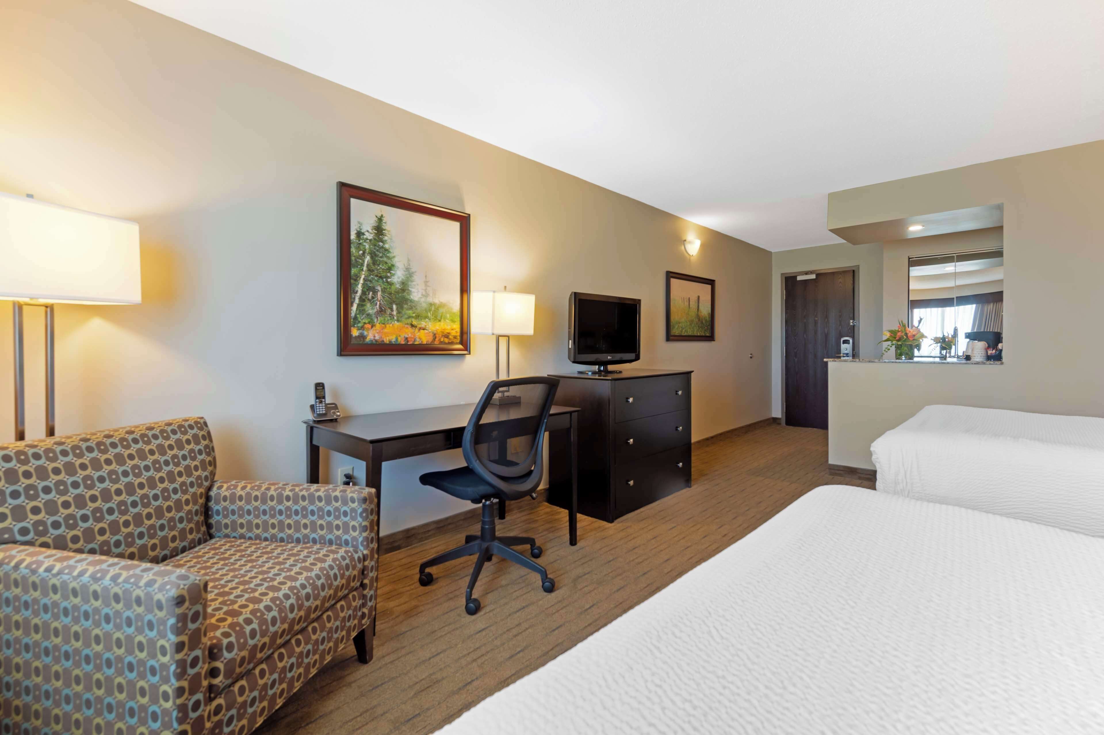 A hotel room with a bed, a desk with a chair, a television, and a dresser.