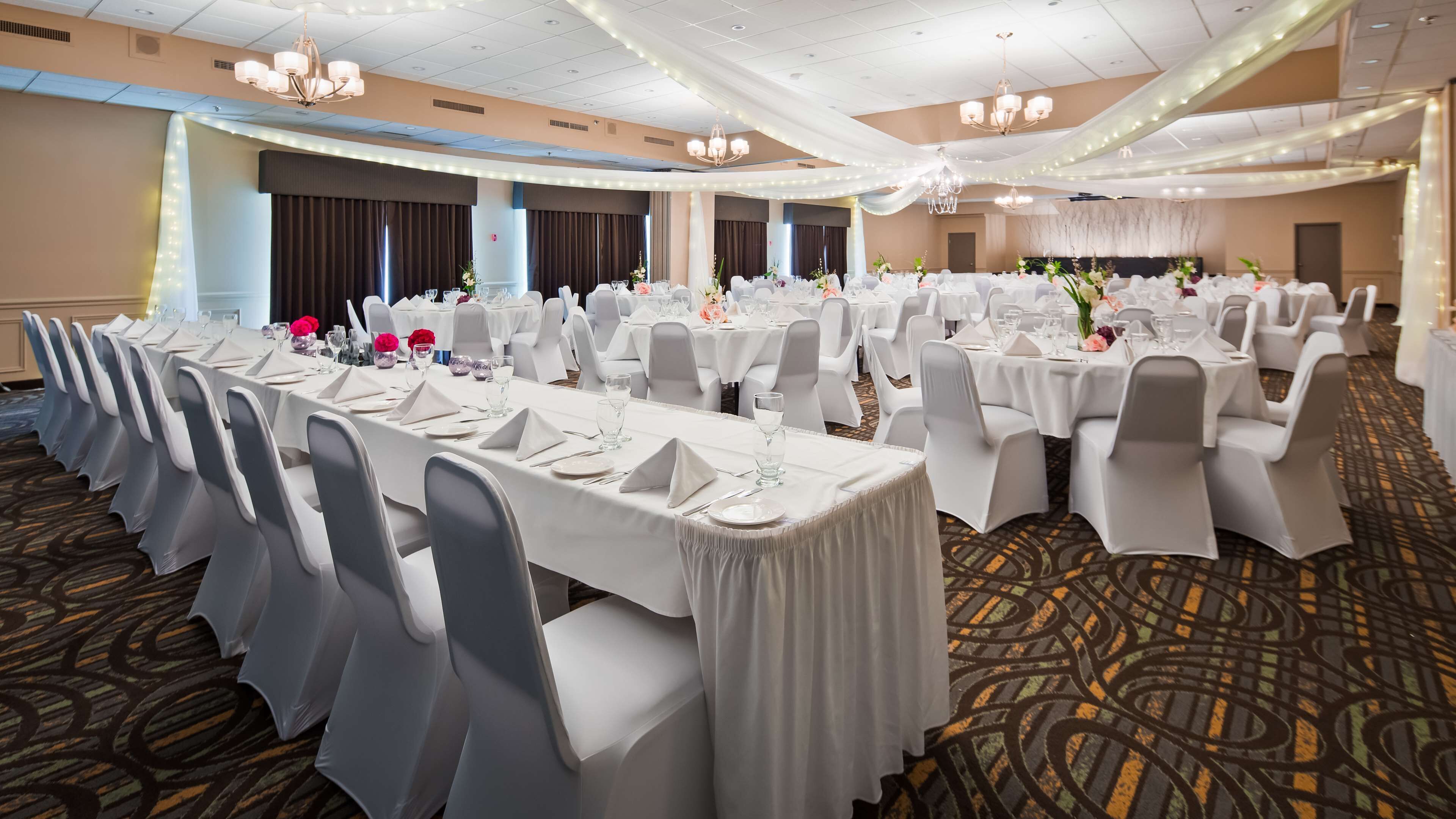 Un salón de banquetes con mesas redondas, manteles blancos y sillas grises.