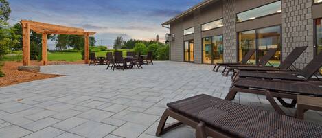A patio area with outdoor seating, a pergola, and a modern building with large windows.