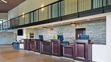 A spacious lobby with a high ceiling, a staircase with a black railing, and a stone wall.