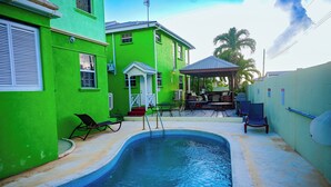 A swimming pool with lounge chairs, a covered seating area, and a building with a green exterior. - Best E Villas Prospect (Prospect)