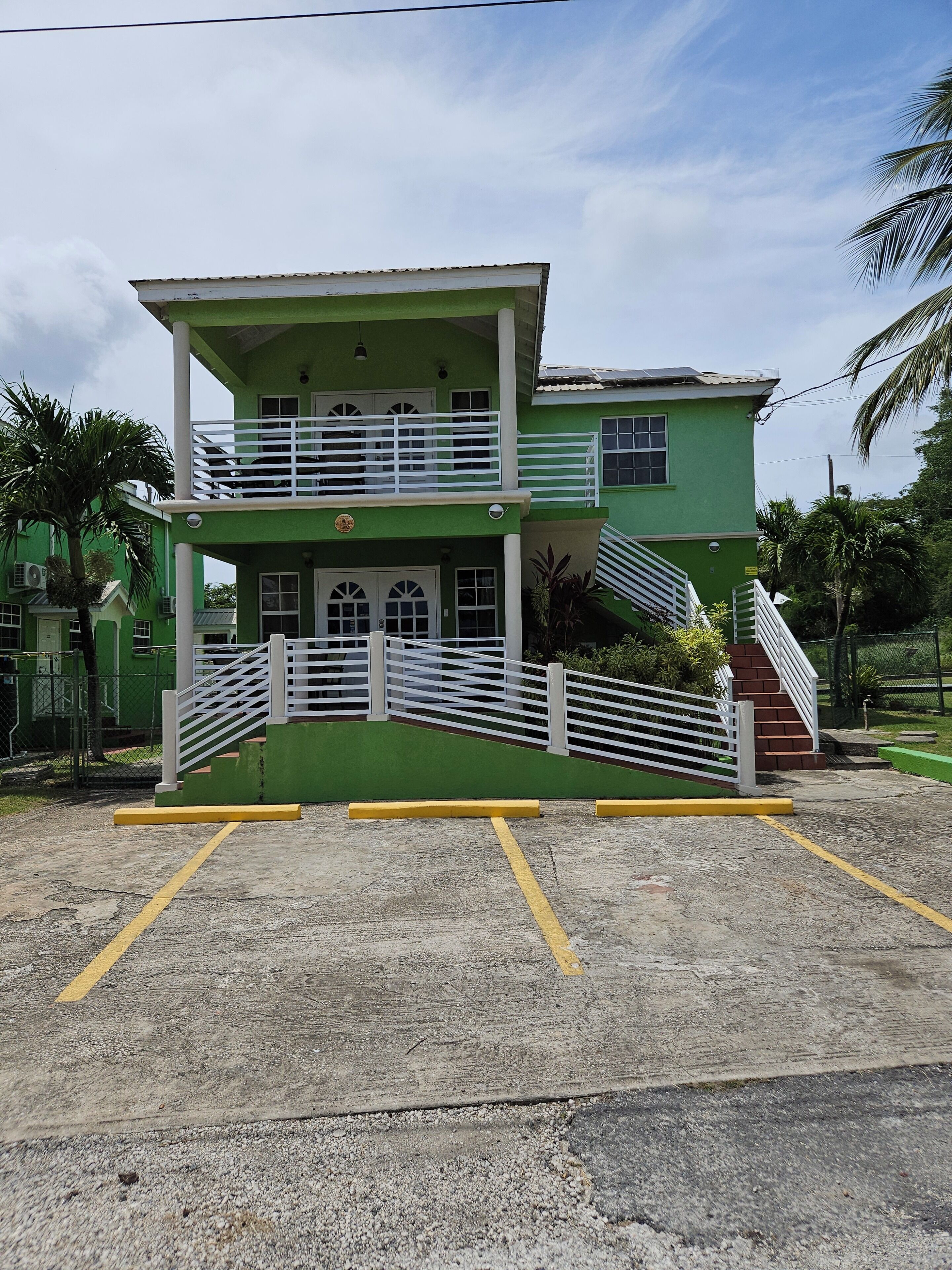Um edifício de dois andares com fachada verde, guarda-corpos brancos e escadaria que leva ao andar superior.