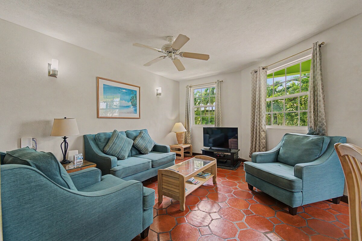 A living room with a ceiling fan, a television, and a large window with curtains.