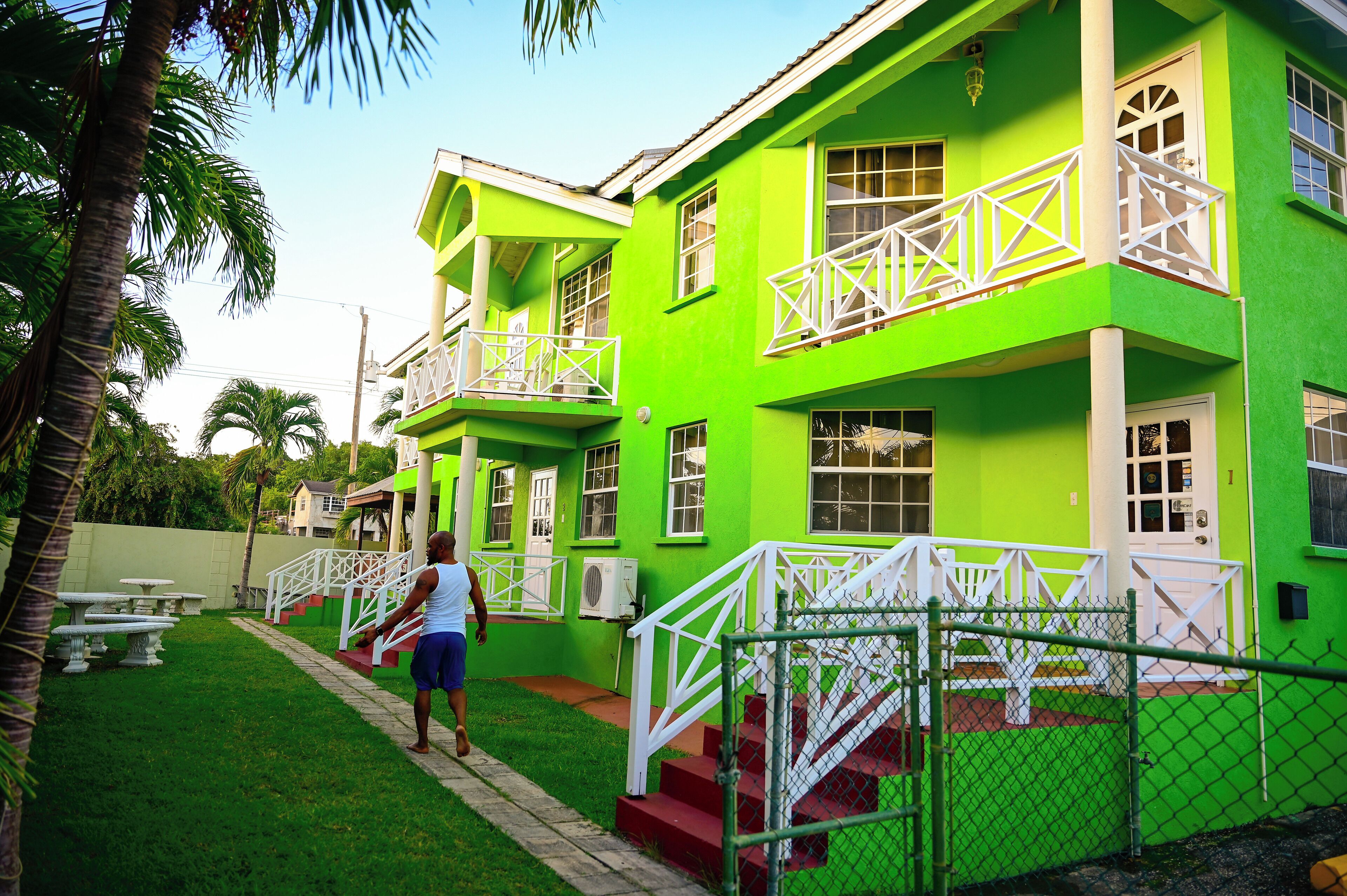 A two-story building with a bright green exterior, white railings, and a red staircase leading to the entrance.