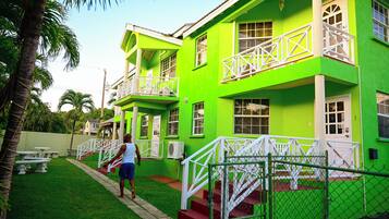 A two-story building with a bright green exterior, white railings, and a red staircase leading to the entrance.