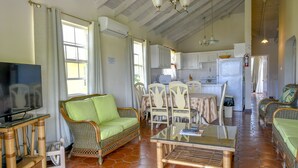 A living room with a television, wicker sofa, dining table, chairs, and a kitchen area with cabinets and appliances. - Best E Villas Prospect (Prospect)