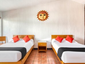 A hotel room with two beds, each with a wooden headboard, white bedding, and red pillows. There is a small wooden nightstand between the beds, and a decorative sun-shaped wall art above the headboard. - Hotel Arana Tonalá (Tonalá)