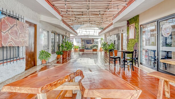 A spacious indoor area with a long wooden table, potted plants, and a high ceiling with exposed beams and lighting fixtures. - Hotel Arana Tonalá (Tonalá)