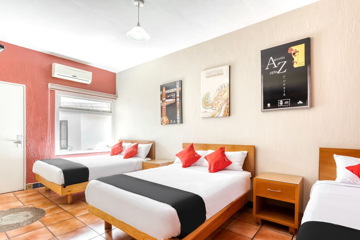 Habitación de hotel con dos camas, cada una con ropa blanca y almohadas rojas, cabecero de madera, mesita de noche y aire acondicionado de pared.