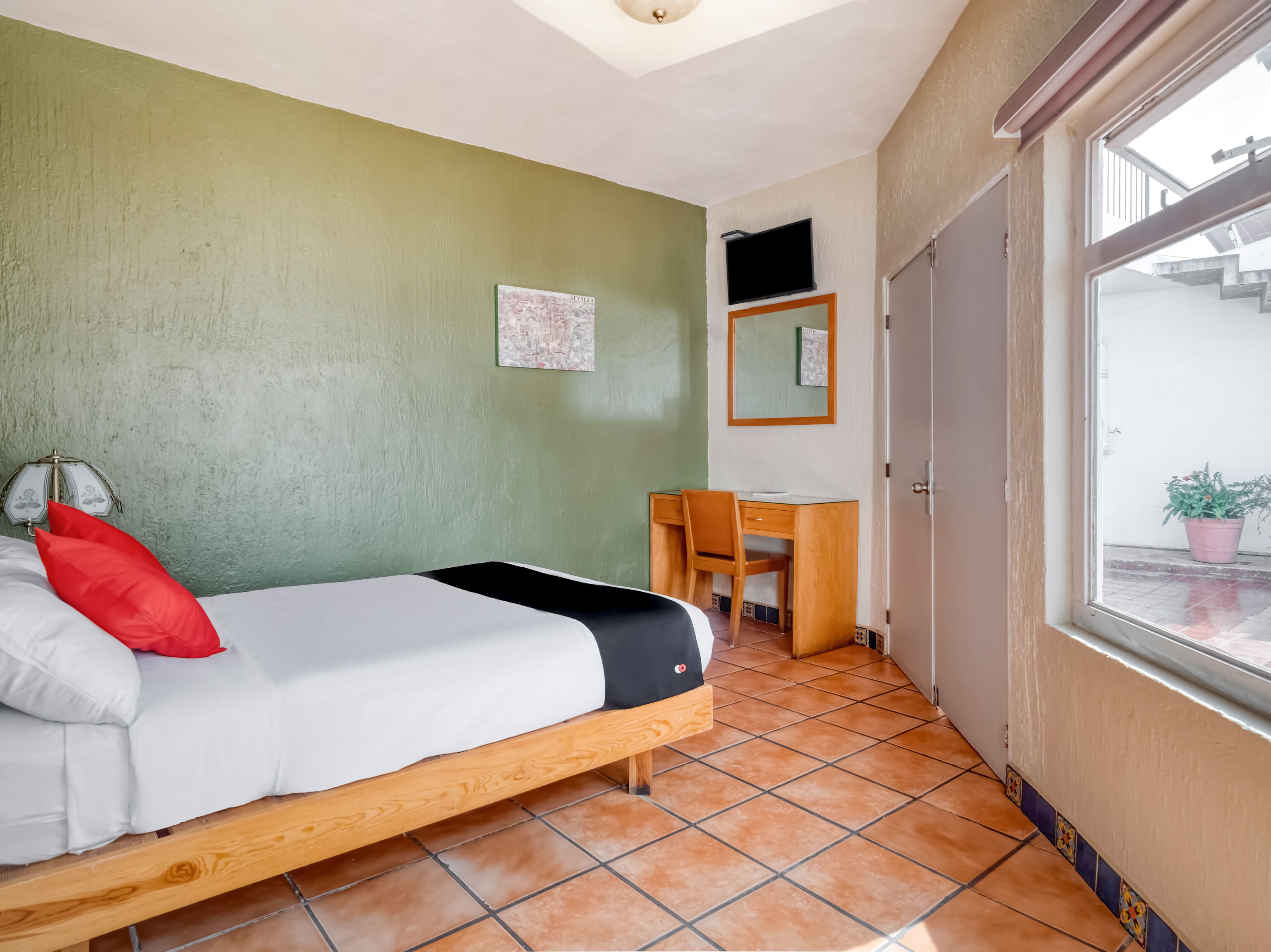 Ein Zimmer mit einem Bett, einem Schreibtisch, einem Sessel, einem Fernseher und einem Fenster.