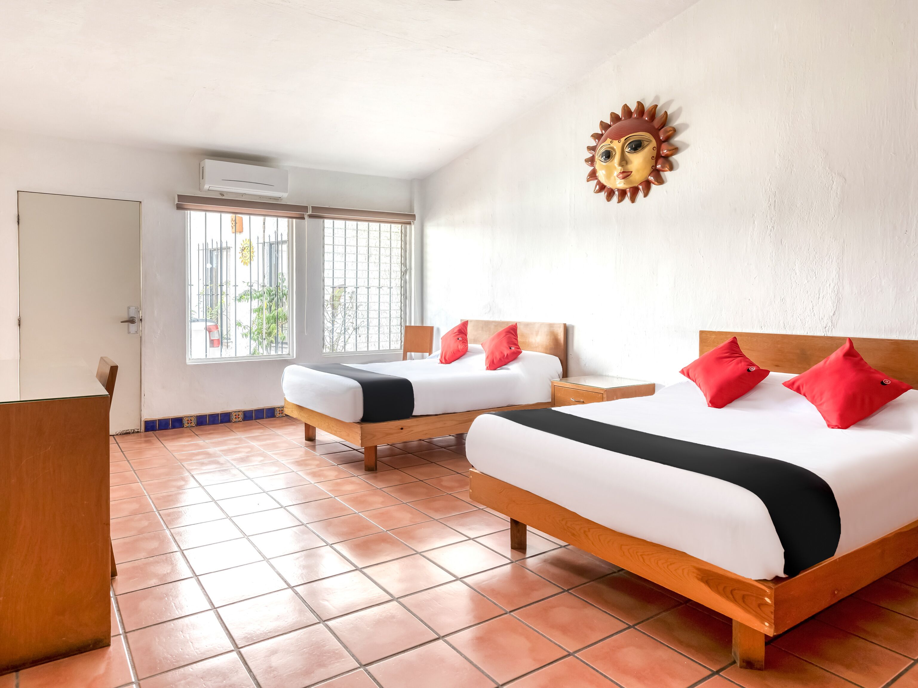 A hotel room with two beds, a wooden headboard, a red sun decoration, and a window with a view of greenery. - Hotel Arana Tonalá (Tonalá)