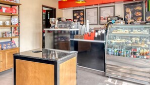 A modern cafe interior with a coffee machine, shelves with cups, and a display case with pastries. - Hotel Arana Tonalá (Tonalá)