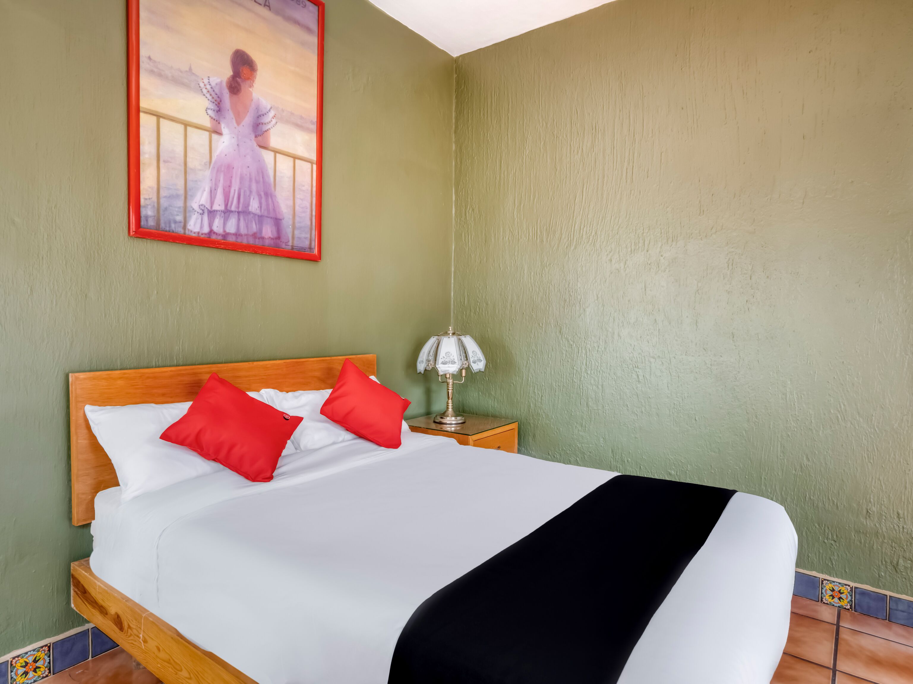 Una cama bien tendida con almohadas blancas y rojas, un cabecero de madera y una manta de color negro.