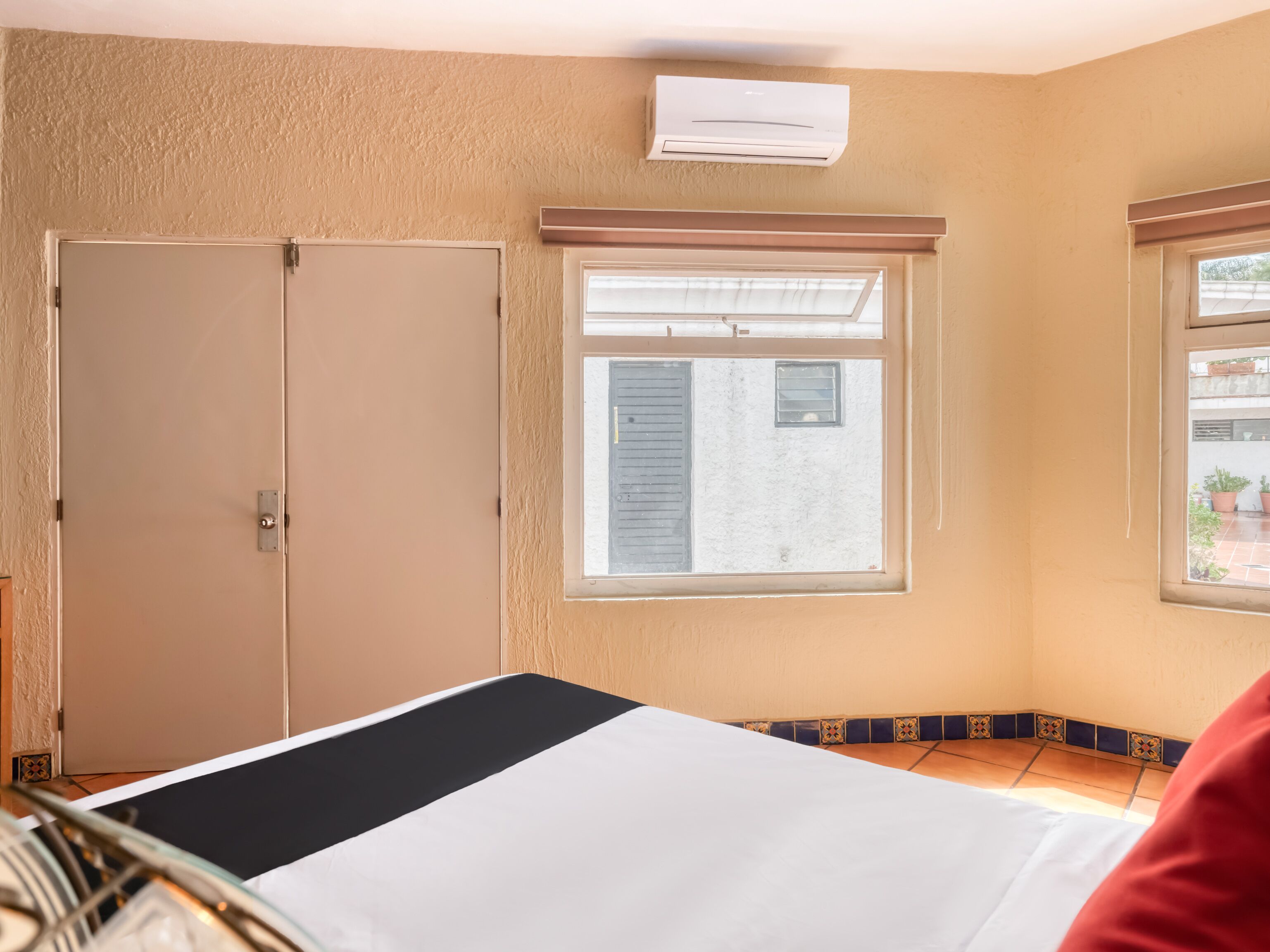 Ein Hotelzimmer mit Bett, Kleiderschrank, einem Fenster mit Jalousien und einer Klimaanlage.