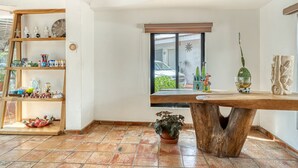 A room with a wooden table, a shelf with various items, a window with a view of a car and greenery, and a potted plant. - Hotel Arana Tonalá (Tonalá)
