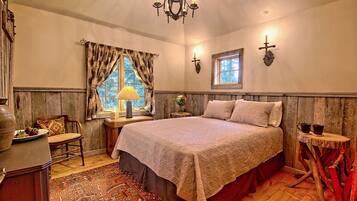 A bedroom with a large bed, wooden walls, a chandelier, a window with curtains, and a small table with a lamp.