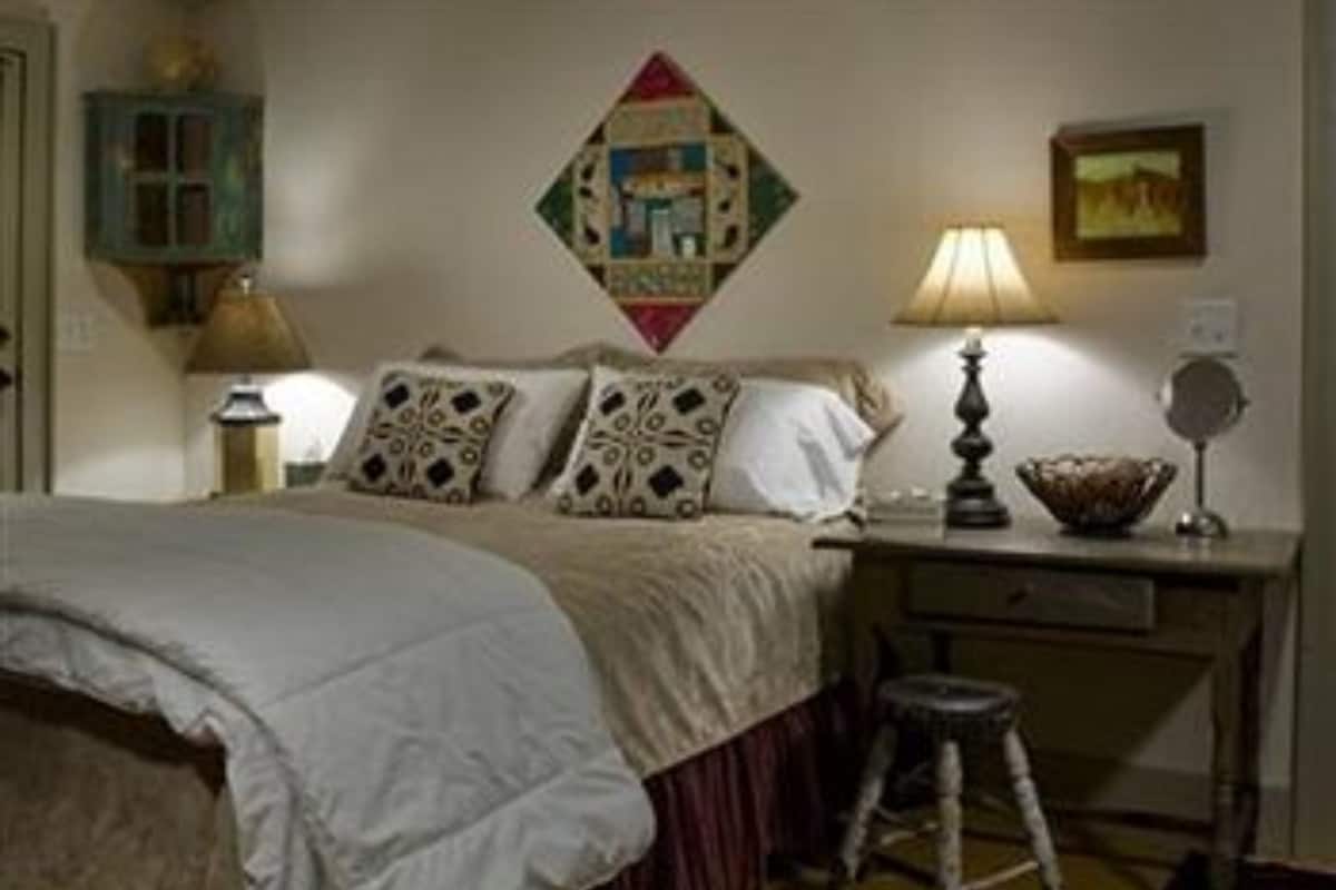 A bedroom with a bed, a nightstand, a lamp, a mirror, and a wall decoration.
