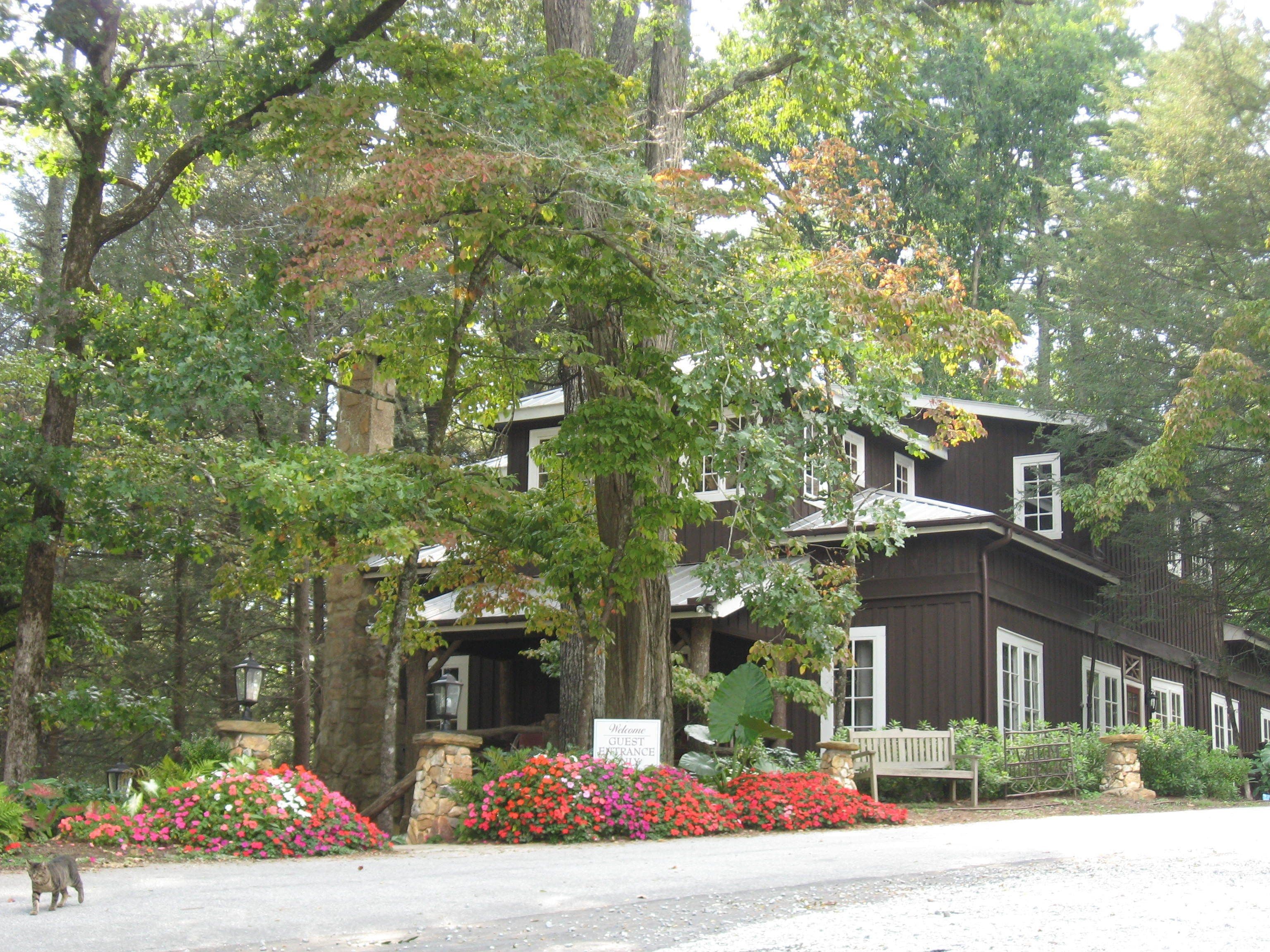 A large, historic building with a stone entrance, surrounded by lush greenery and vibrant flowers.
