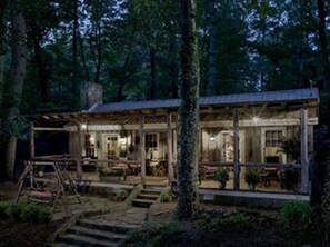 A rustic cabin with a covered porch, surrounded by trees.
