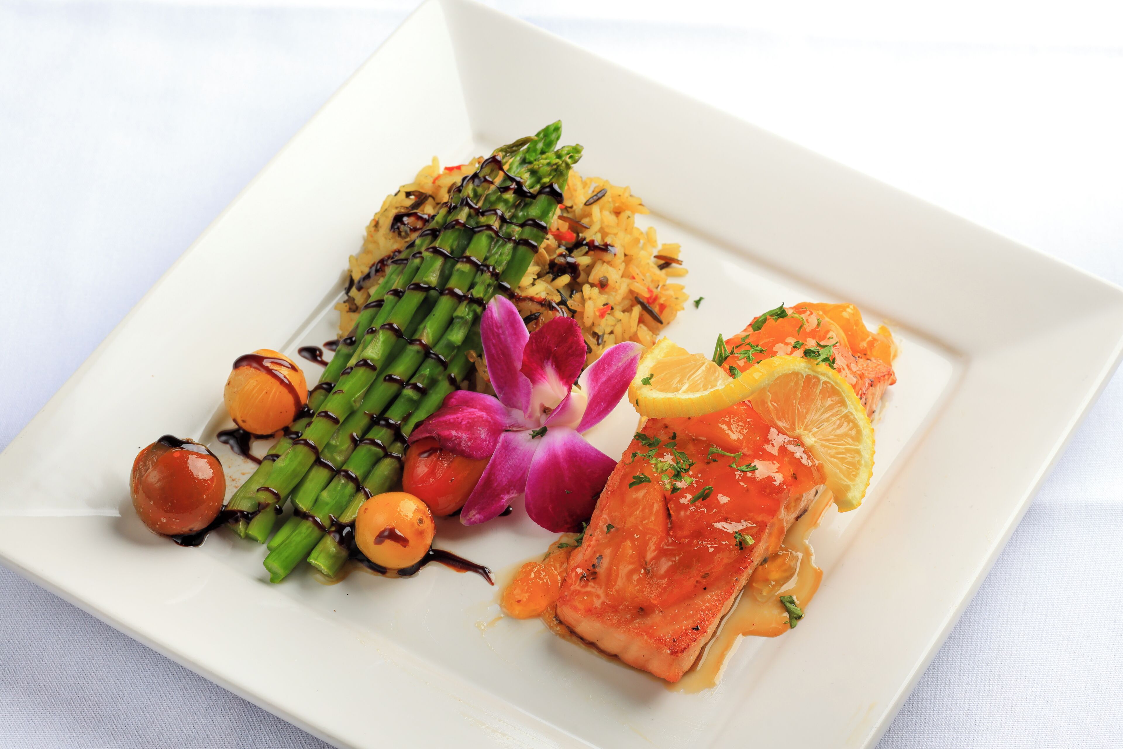 Ein weißer Teller mit Lachs, Spargel und einer violetten Blume.