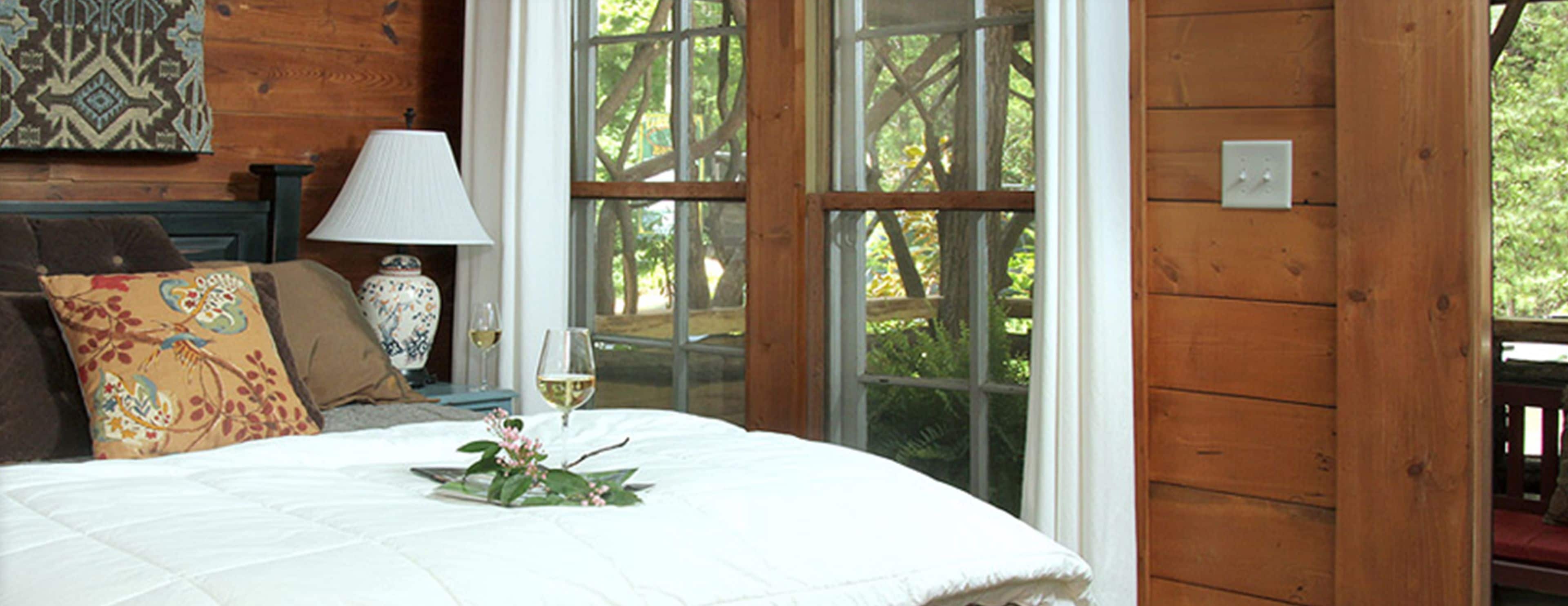 Un dormitorio con cama, mesita de noche, lámpara y ventana con vista a árboles.