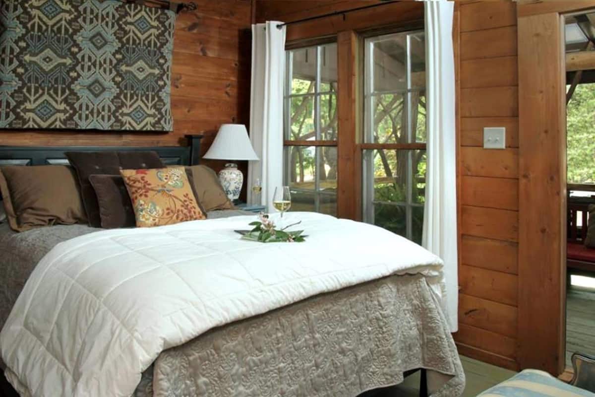 A cozy bedroom with a large bed, a patterned wall hanging, and a view through a window.