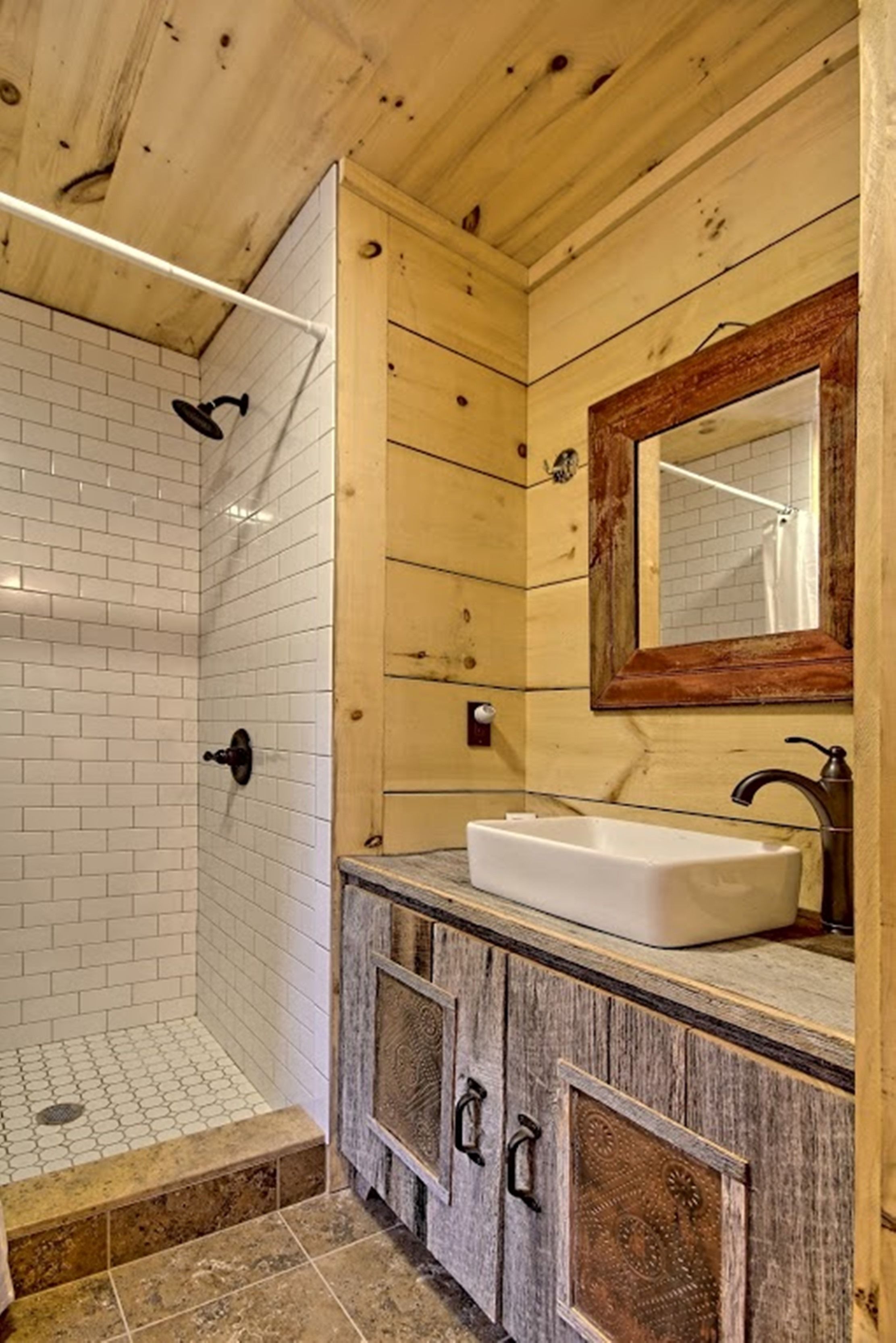 Une salle de bain avec des murs recouverts de carreaux blancs, un plafond en bois, un grand miroir et un lavabo blanc.