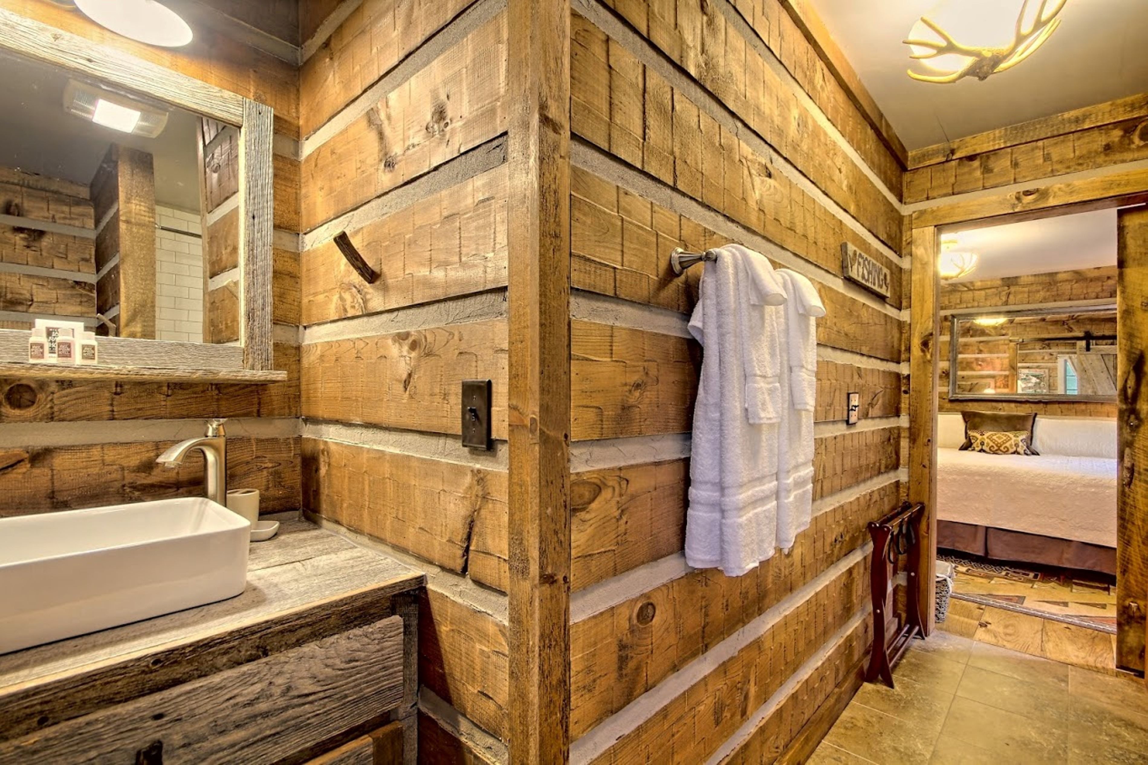A rustic wooden bathroom with a large mirror, a sink, and a towel rack.
