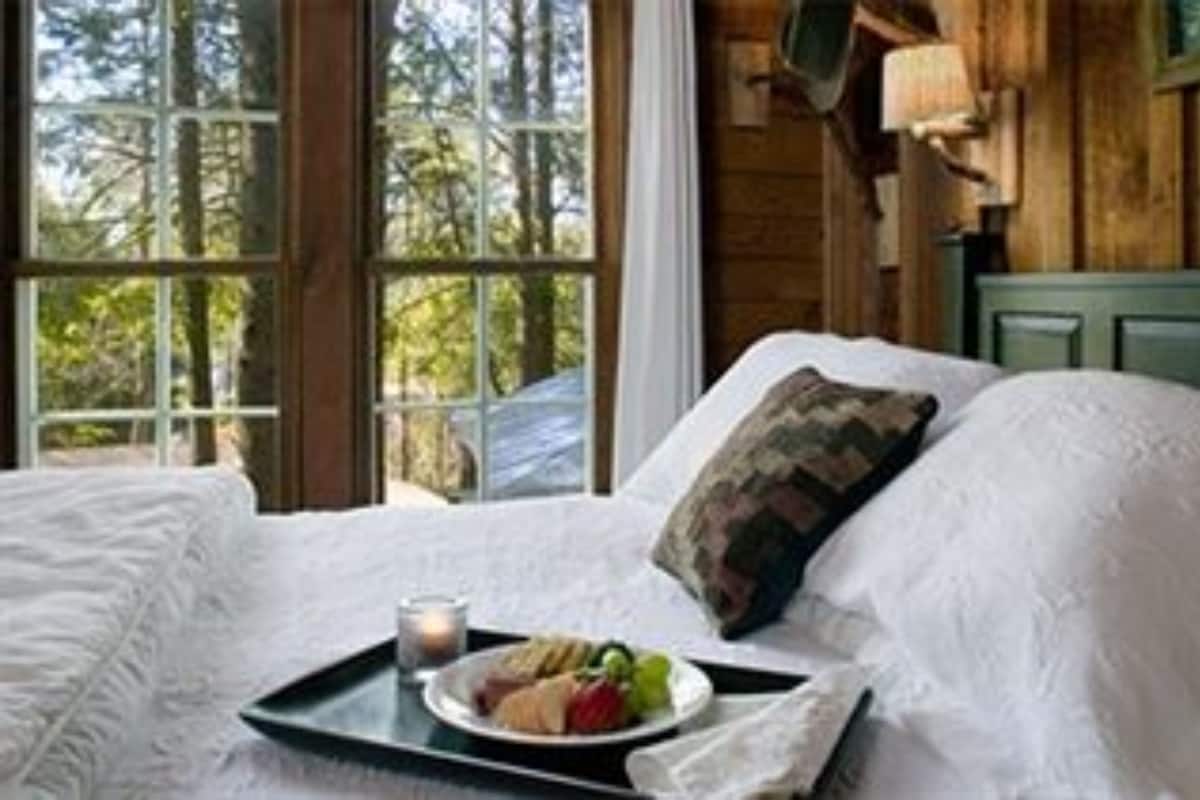 A bed with white linens, a tray with food, and a window with a view of trees.