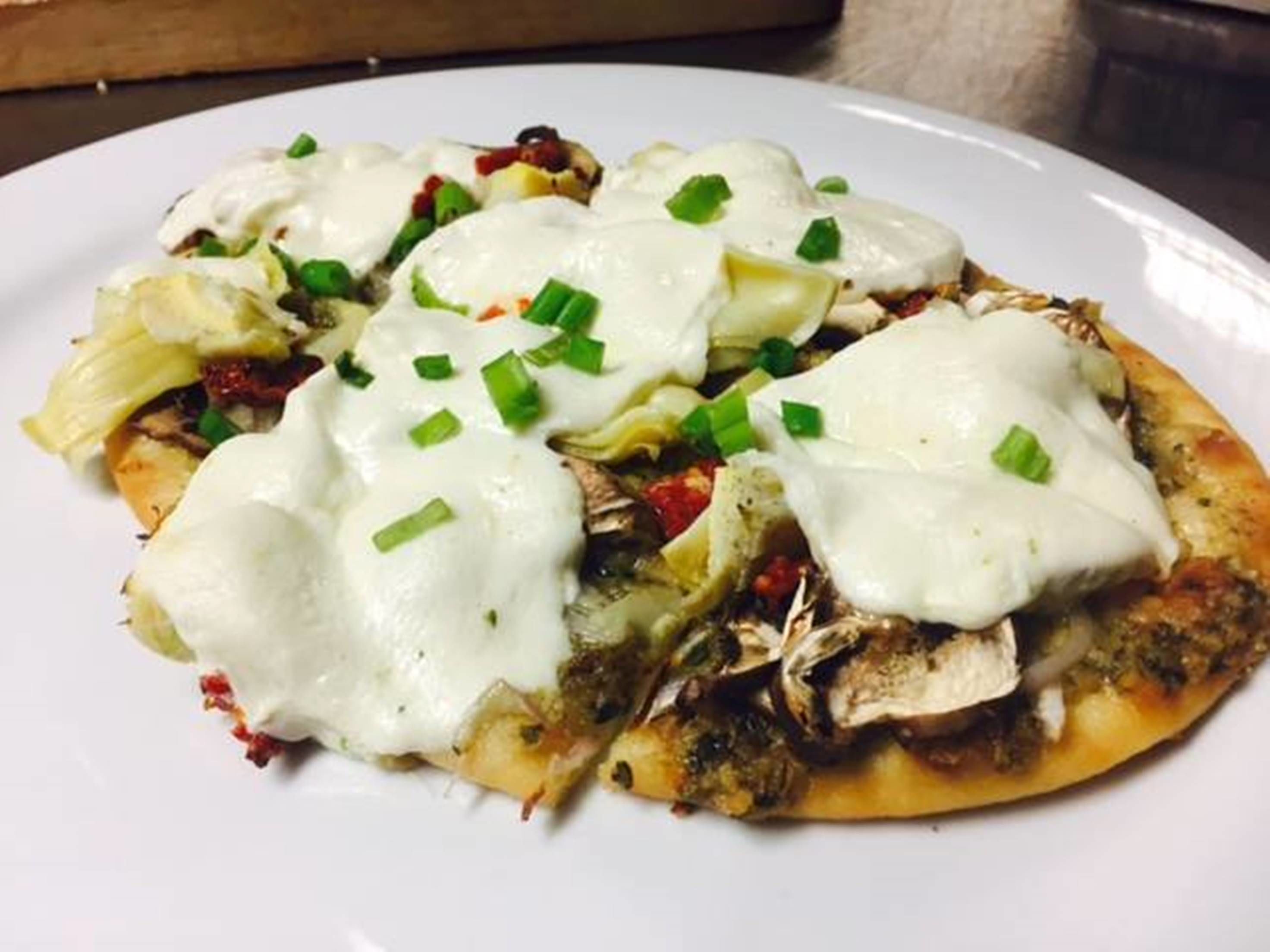 A plate of food with a white sauce, green onions, and pieces of meat on a flatbread base.